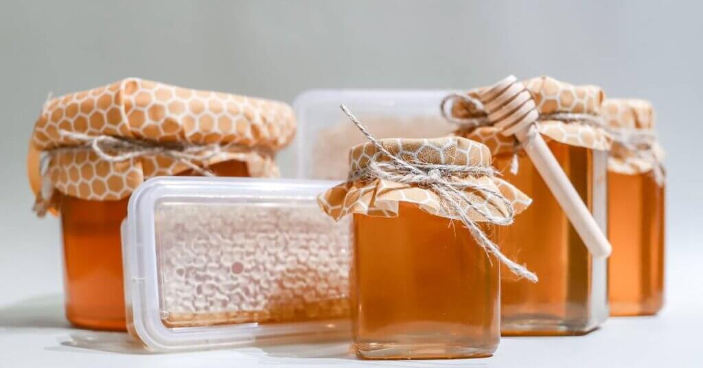 A collection of glass and plastic honey containers in different shapes and sizes. Some are decorated with fabric and twine.