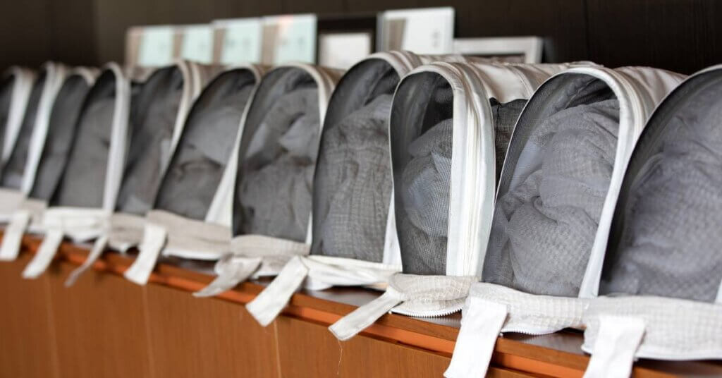 Several white beekeeping veils with suits folded inside of them. They are stored in a row on a wooden shelf.