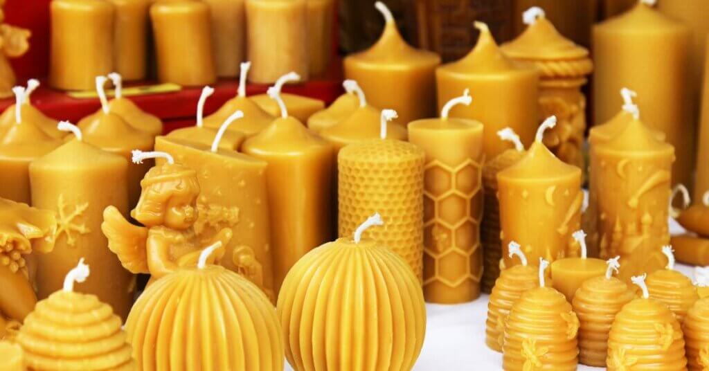 A collection of golden beeswax candles. Some are plain while others feature designs like hives, honeycomb, angels, and more.